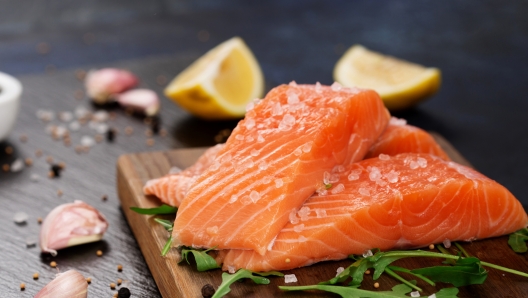 Raw fillet of salmon with sea salt, lemon and pepper on black stone background. Fresh fish prepared for cooking. Top view, copy space. Healthy Brain Food concept.