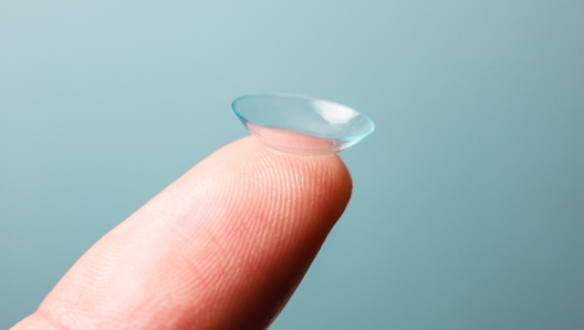 A Contact lens is resting on a finger against a blue background