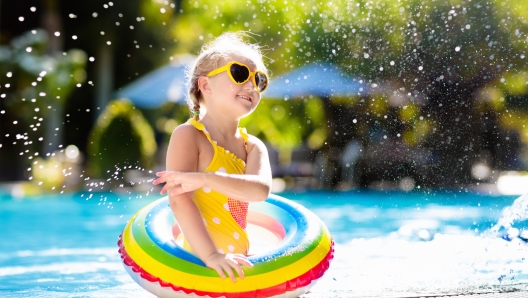 Child with goggles in swimming pool. Little girl learning to swim and dive in outdoor pool of tropical resort. Swimming with kids. Healthy sport activity for children. Sun protection. Water fun.