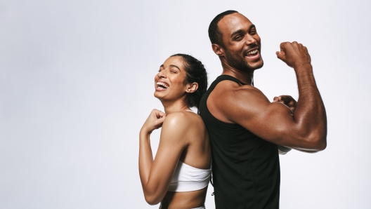 Smiling fitness couple standing back to back against white background. Fit couple showing arm muscles standing together.