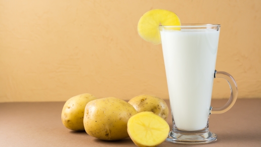 Alternative vegan vegetable potato milk in a glass and potato tubers next on a brown background. Vegetarian and flexitarian food.