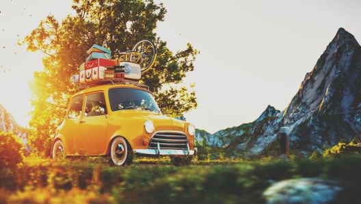 Cute little retro car with suitcases and bicycle on top goes by wonderful countryside road at sunset