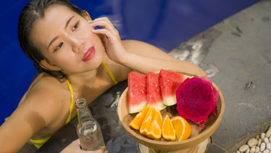 outdoors Summer lifestyle portrait of young beautiful and happy Asian Korean woman in bikini enjoying vacation at swimming pool relaxed and cheerful bathing at villa or luxury tropical resort