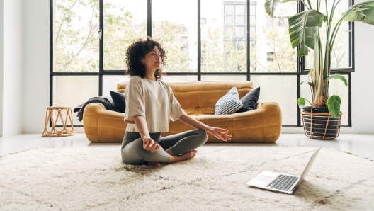 Young multiracial latina woman meditating at home with online video meditation lesson using laptop. Meditation and spirituality concept.