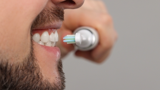 Man brushing his teeth with electric toothbrush on light grey background, closeup. Space for text