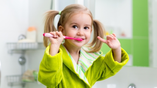 Smiling kid child girl brushing teeth in bathroom