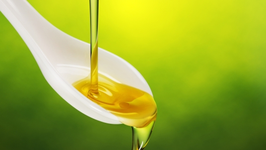 extra virgin olive oil poured in a spoon overflowing on green background