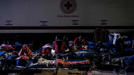 TOPSHOT - Migrants rest on camp beds as they wait on the Italian island of Lampedusa, on September 14, 2023, as authorities prepare to move them to Sicily. Over 6.000 migrants arrived on the Italian island of Lampedusa in the last 36 hours, according to the Italian Red Cross. Police started to move some of the migrants to Sicily by ferry and plane. (Photo by alessandro serrano / AFP)