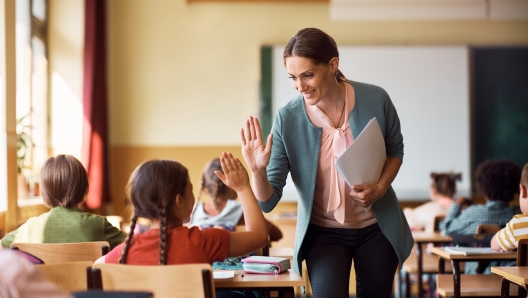 Happy elementary school teacher giving high-five to her student during class in the classroom.