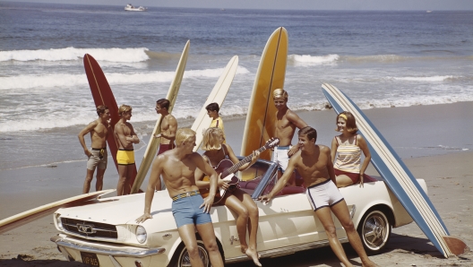 A group of surfers on a beach with a Ford Mustang car.