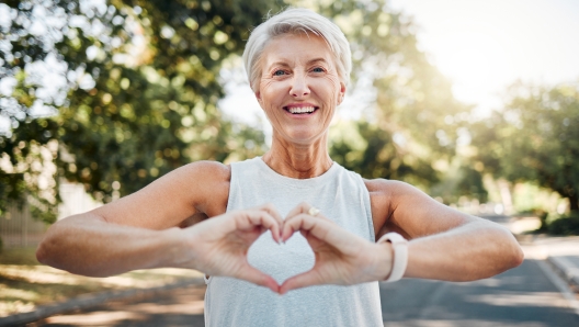 Fitness, happy and heart hands of old woman in nature after running for health, wellness and workout. Smile, motivation and peace with senior lady and sign for love, faith and training in nature