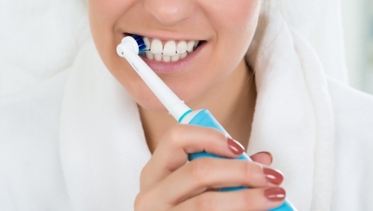 Close-up Of A Young Woman In Bathrobe Brushing Teeth With Electric Toothbrush