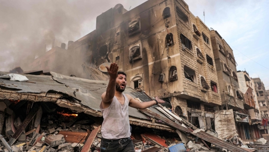 TOPSHOT - A man reacts outside a burning collapsed building following Israeli bombardment in Gaza City on October 11, 2023. At least 30 people have been killed and hundreds wounded as Israel pounded the Gaza Strip with hundreds of air strikes overnight, a Hamas government official said on October 11. The Israeli military confirmed it had hit several Hamas targets during the night in the Palestinian enclave. (Photo by MOHAMMED ABED / AFP)