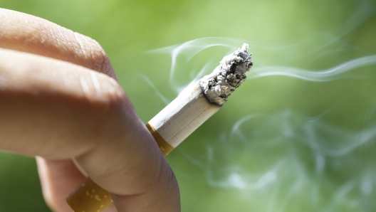 cigarette smoking. cigar burning between the fingers of an outdoor tobacco smoker. cigarette smoker burning to the end with white smoke.