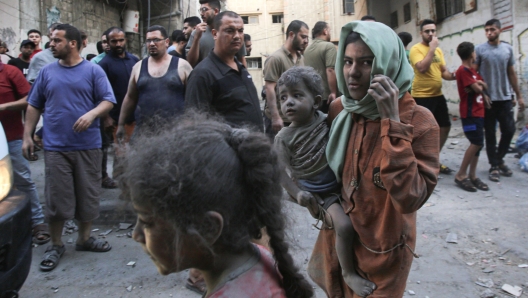 A Palestinian woman covered in dust and dirt carries a child, as raging battles between Israel and the Hamas movement continue for the sixth consecutive day Gaza City on October 12, 2023. Israel continued to pound Gaza on October 10, 2023,  vowing to "destroy" Hamas on the sixth day after the militants' unprecedented surprise attack. (Photo by BASHAR TALEB / AFP)