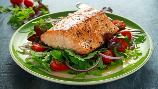 Baked salmon steak with tomato, onion, mix of green leaves salad in a plate. healthy food.