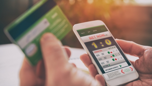 Man betting on sports with credit card, over shoulder view on hand with smartphone