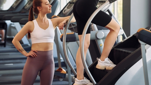 Trainer helping to run the racetrack. Two women in sportive clothes have fitness day in the gym together.