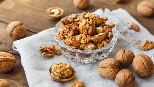 Glass bowl with walnuts on rustic homespun napkin. Healthy snack on old wooden background.