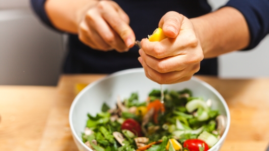 Woman hands squeezing fresh lemon juice into salad bowl on a wooden kitchen table