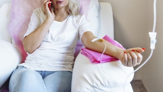 Woman in hospital talking at mobile phone while needle is in arm, Vitamin Therapy Iv Drip Infusion In Women Blood