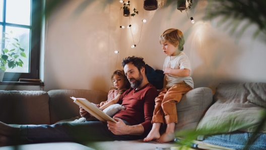 A mature father with two small children resting indoors at home, looking at photo album.