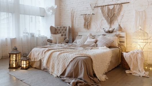 Side view of lovely bedroom with plaid and pillows on comfortable bed, home decor and cushions on soft armchair in white interior design in bohemian style