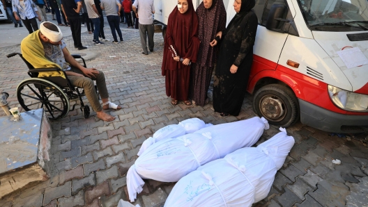 Women stand next to the bodies wrapped in shrouds of family members killed during an Israeli military strike as they are taken for burial from the Al-Aqsa hospital in the town of Deir Al-Balah, in the central Gaza Strip, on October 15, 2023. Israeli forces were on October 15, readying for a looming Gaza ground invasion aimed at destroying Hamas, the Palestinian Islamist militant group that unleashed the bloodiest attack in the country's history. (Photo by Mahmud HAMS / AFP)