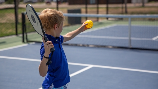 Young caucasian boy playing pickle ball on a hot summer day.