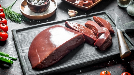 Sliced raw liver with tomatoes, herbs and spices. On dark rustic background