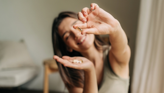 Happy smiling woman holding an omega pill in her hand.