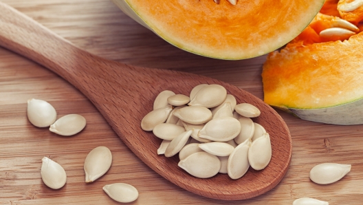 Pumkin seeds inside of wooden spoon near the pumpkin. Close up. Diet concept.