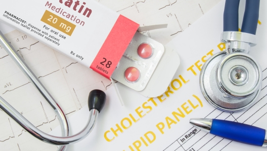 Effects and treatment of statins concept photo. Open packaging with drugs tablets, on which is written "Statin Medication", lies near stethoscope, result analysis on cholesterol (lipid panel) and ECG