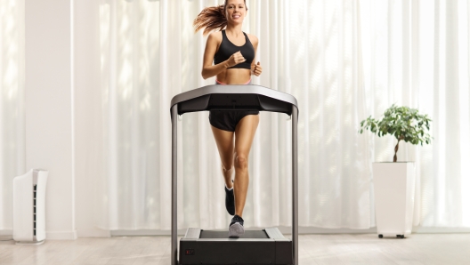 Full length portrait of a young woman in shorts and top running on a treadmill at home