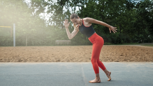 Athletic sexy middle-aged woman, doing fitness barefoot on the volleyball court.