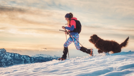 Sporty girl with her dog during an alpine trekking on the snow