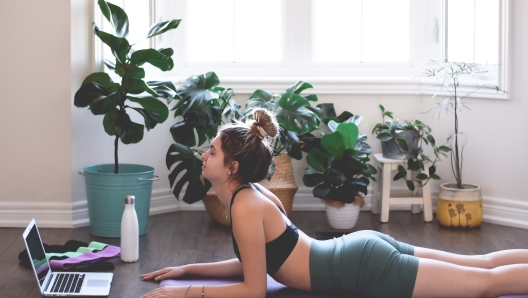 Young woman in yoga cobra pose working out at home using online workout video on laptop computer as a reference