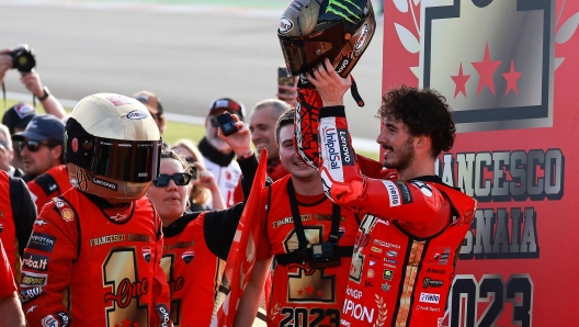 Ducati Italian rider Francesco Bagnaia (R) racts raising his helmet to winning the MotoGP Valencia Grand Prix at the Ricardo Tormo racetrack in Cheste, on November 26, 2023. Italy's Francesco Bagnaia enjoyed a dream day as he retained his MotoGP world title and crowned it with victory in the final race of the season in Valencia today. The 26-year-old Ducati rider had been assured of the championship when his sole rival Jorge Martin crashed early in the race. (Photo by JOSE JORDAN / AFP)