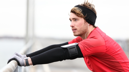 Male runner stretching after running in cold fall weather wearing warm sporty running clothing. Handsome male fitness sport model outdoors.