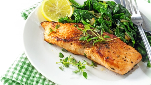 grilled salmon with thyme, lemon and spinach on a plate, vegetarian low carb dish, green white napkin on a white background, selected focus, narrow depth of field