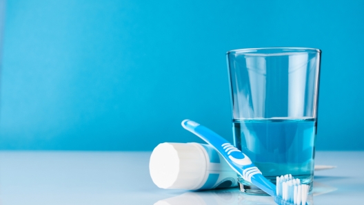 A blue toothbrush with toothpaste and glass of blue mouthwash on blue background with copy space, close-up. Dental oral hygiene concept