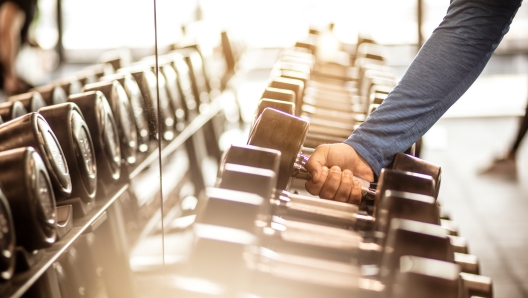 Time to pump that iron. Muscular build sportsman taking weights from a rack in a gym. Focus is on hand. Close up.