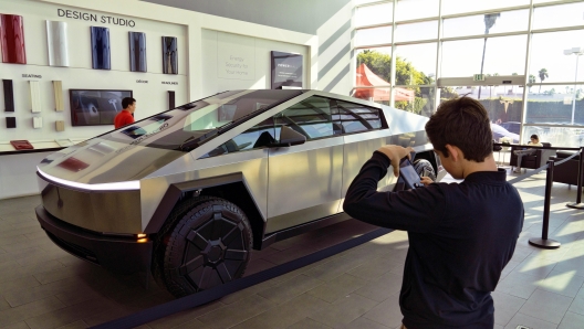 A visitor to Tesla takes a photo of a Tesla Cybertruck on display in the showroom in Buena Park, Calif., Sunday Dec. 3, 2023. With manufacturing kinks still to be worked out, Tesla has delivered the first dozen or so of its futuristic Cybertruck pickups to customers. (AP Photo/Richard Vogel)