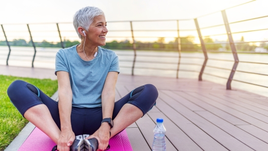 Senior woman exercising in park while listening to music. Senior woman doing her stretches outdoor. Athletic mature woman stretching after a good workout session.