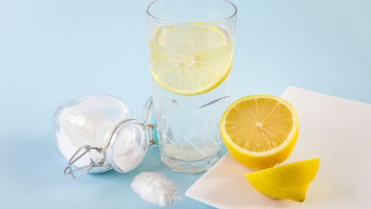 Baking soda in drinking glass with water and lemon slice juice, health benefits for digestive system concept. Light blue background.