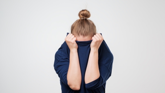 European woman hiding face under the clothes. She is oulling sweater on her head. Depressed emotion. Wish to be alone.