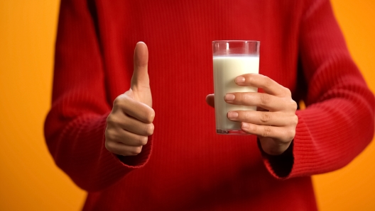 Female holding glass of fresh milk showing thumb up, diary refreshment, calcium