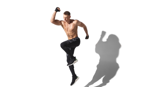 Running, jumping high. Stylish young male athlete on white studio background, portrait with shadows. Sportive fit model in motion and action. Body building, healthy lifestyle, style concept.