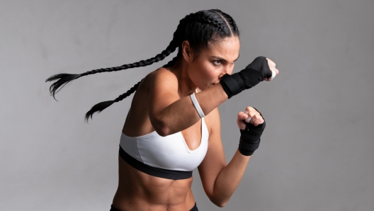 Determined middle aged woman boxer preparing for boxing fight. Fitness mid adult woman preparing for boxing training at gym. Beautiful strong sportswoman in boxing gloves prepared right hand punch.