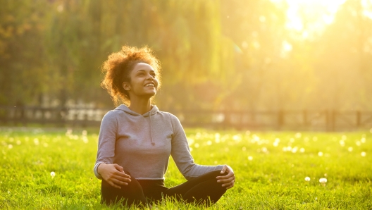 Happy young woman sitting outdoors in yoga position